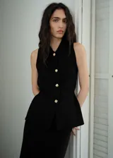 Chaleco negro sin mangas con cuello camisero, botones dorados con diseño de joya y corte entallado.