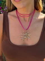Gargantilla con dije de sol dorado y cordón fucsia ajustable.