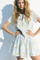 Vestido corto de algodón con estampado floral en tonos celeste y verde, con escote redondo con abertura en V y lazos finos con cuentas en los extremos.