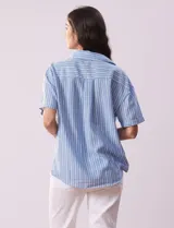Blusa celeste y blanca a rayas verticales, con cuello con solapa y escote en V. Delantera cruzada con abertura simulada y mangas cortas.