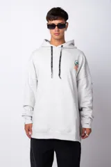 Buzo canguro gris claro de corte oversize, con capucha y cordones negros con letras blancas. Presenta un bolsillo tipo canguro y un estampado pequeño en el pecho y otro en la manga.