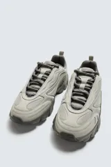 Zapatillas deportivas color crema con cordones, suela gruesa con diseño irregular y detalles en gris.