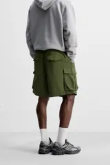 Bermuda color verde militar, relaxed fit, confeccionada en tejido técnico ligero. Cintura elástica ajustable con cordón interior, pliegues frontales, bolsillos delanteros y traseros con solapa, bolsillos cargo con solapa en perneras. Cierre frontal con cremallera y botón.