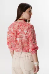 Camisa roja con estampado floral, cuello en V y mangas largas con puños abotonados.