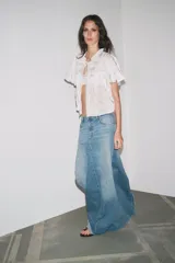 Falda larga de denim azul, de tiro alto, con trabillas y cinco bolsillos. Cierre frontal con cremallera y botón metálico.