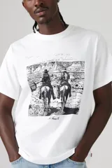 Remera blanca de corte recto con cuello redondo y estampado frontal de dos jinetes cabalgando en un paisaje desértico.