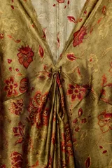 Vestido largo de seda, color verde oliva con estampado floral en tonos rojos y terracota. Presenta escote pico con ajuste fruncido en el delantero y mangas amplias tipo murciélago.