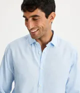 Camisa celeste de lino con cuello camisero, abotonadura frontal y mangas largas.