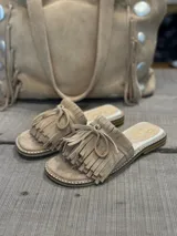 Sandalias bajas color beige de gamuza, con detalle de flecos y lazo en la tira delantera.