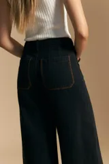 Jean de corte wide leg y tiro alto, color negro con costuras en contraste color ocre. Presenta bolsillos delanteros y traseros con detalle de pespunte, y ruedo ancho con costura decorativa.