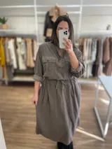 Vestido camisero largo color gris topo, de pana fina con línea italiana, cuello mao, cierre frontal con botones, mangas largas con puños abotonados, dos bolsillos de parche en el pecho, cintura ajustable con cordón y falda recta.