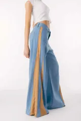 Pantalón de jean celeste de pierna ancha con cortes en los laterales que van desde la pretina al bajo del pantalón. Presenta godets triangulares en tela color beige con bordado floral para darle mayor amplitud y detalles a la prenda.