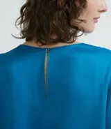 Blusa celeste de viscosa con textura satinada, cuello redondo, manga corta con sisa desplazada y abertura en la espalda.