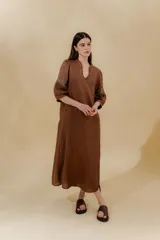 Vestido largo color beige, confeccionado en lino, con escote en V con volados y apliques de puntilla en las mangas. Posee bolsillos delanteros y tajos laterales.