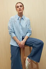 Camisa celeste de manga larga con cuello camisero y botones de nácar. Presenta detalles de broderie calado en el canesú y las mangas.