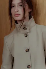Chaqueta color beige de corte recto, cuello alto estructurado y cierre frontal con botones marrones.