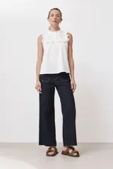 Top blanco sin mangas con cuello alto, detalle de broderie y volados.