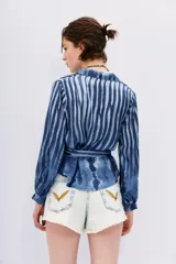 Camisa celeste con rayas verticales blancas, de corte holgado y mangas largas abullonadas con puños elásticos. Tiene cuello camisero, cierre frontal con botones y lazo en la cintura.