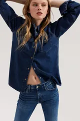 Camisa de denim azul con cuello clásico, cierre frontal con botones a presión, dos bolsillos con solapa abotonada en el pecho, mangas largas con puños abotonados y canesú en la espalda.
