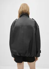 Anorak negro oversize con cuello alto, cierre frontal con botones y cremallera oculta, mangas largas con puños abotonados y bolsillos laterales con cremallera.