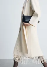 Abrigo largo color crema, con cuello con solapa, lazo a la cintura, bufanda desmontable y terminación de flecos.