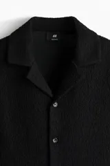 Camisa de manga corta negra con textura, cuello abierto, tapeta lisa y bajo recto.