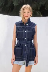 Chaleco de jean azul oscuro con cuello camisero, sin mangas, con bolsillos frontales y cinturón de la misma tela.