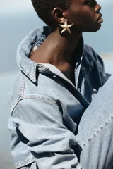 Camisa corta de denim celeste, con cuello solapa, manga larga, bolsillo delantero de plastrón y cierre frontal con botones metálicos.