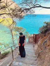 Vestido largo tejido de algodón color negro, sin mangas, con cuello redondo y tajos laterales. Presenta dos bolsillos de cuero color marrón en el frente.