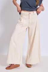 Pantalón de jean color crudo, de corte palazzo y tiro alto, con bolsillos laterales y traseros. Se ajusta a la cintura con cinturón de cuero marrón con hebilla dorada.