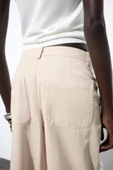 Pantalón color beige de tiro alto, corte ancho y largo midi, con pinzas delanteras, bolsillos laterales y traseros. Cierre frontal con cremallera y botón.