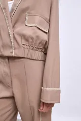 Cazadora color beige con bordados en hilo blanco en cuello, bolsillos y puños.