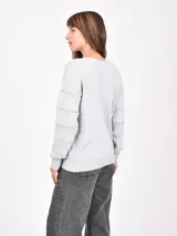 Buzo de tejido de punto negro, con cuello en V y mangas largas. Presenta franjas horizontales con pequeños calados decorativos.