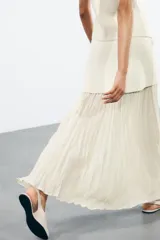 Falda midi color crema, de tiro alto con cintura elástica y tejido plisado semitransparente.
