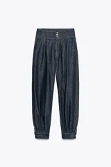 Pantalón bombacho de denim azul oscuro, tiro alto, con bolsillos delanteros y puños con botón en los tobillos. Cierre frontal con cremallera y botones metálicos.