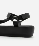 Sandalia flatform negra de material sintético, con punta redonda y tiras torcidas.