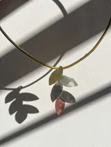 Gargantilla rígida dorada con dije de cinco hojas de diferentes metales: alpaca, bronce y cobre.