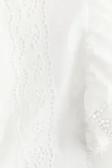 Blusa blanca de algodón con secciones en broderie. Modelo con mangas cortas de volados y cuello redondo con abertura de cerradura y botón oculto en la nuca.