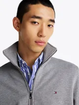 Buzo Tommy Hilfiger de felpa gris con cuello chimenea, cierre de cremallera frontal, bolsillos tipo canguro, puños y bajo de punto canalé, logo bordado en el pecho y corte regular.