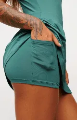 Vestido deportivo color verde con logo bordado en blanco en el pecho. Diseño sin mangas, con cuello mao y cierre parcial con botones. Falda con corte evasé y short interno.