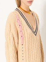 Sweater beige de punto con cuello en V con rayas azul marino y tiras trenzadas rojas y rosas en los laterales.