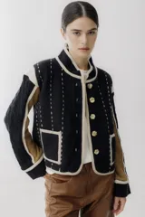 Chaqueta corta de lana color negro con detalles en beige y marrón. Tiene cuello mao, cierre frontal con botones y bolsillos de parche.