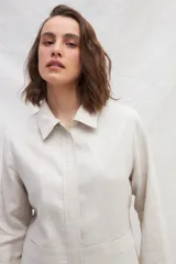 Chaqueta color crema de lino, de corte recto, con cuello camisero y cierre frontal con botones.