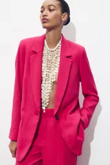 Pantalón de tiro alto color fucsia, con bolsillos delanteros y falsos bolsillos de vivo en la espalda. Tejido con efecto arrugado, pernera recta y cierre frontal con cremallera, botón interior y gancho.