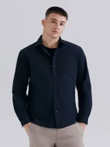 Camisa de vestir azul marino, de corte clásico, con cuello abotonado, manga larga y bolsillo en el pecho.