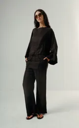 Pantalón negro de tiro alto con elástico en la cintura y pierna ancha. Presenta un pliegue marcado vertical en el frente de cada pierna.