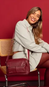 Bandolera bordeaux de cuero sintético con apertura central con cierre metálico. Tiene un bolsillo principal con cierre y un bolsillo frontal con tapa y broches magnéticos. Incluye bolsillos internos y posterior, y correa de galón combinada larga y regulable.