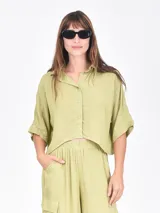 Camisa negra de manga corta, con cuello camisero y botones frontales. Presenta un corte holgado y crop.