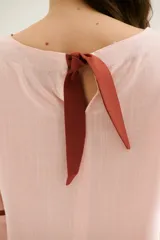 Blusa de lino color celeste claro con cuello redondo y mangas tres cuartos. Presenta un ribete de color marrón oscuro en los puños y un lazo decorativo en el centro del escote.