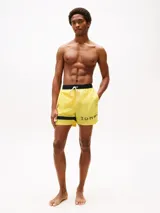 Short de baño amarillo de Tommy Hilfiger, con cintura elástica negra, cordón blanco y logo de la marca en la pierna izquierda.